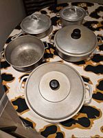 Overview of four aluminum pots with lids on patterned table