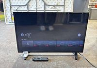 Front view of powered-on 32" Insignia TV with remote placed in front