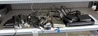 Shelf containing three black external floppy drives, multiple white Apple power adapters and cables, white base station, clear data cartridges