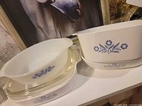 Group view of two oval casseroles, shallow cover dish and two clear lids with blue Cornflower pattern visible