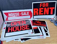 Stack of assorted real estate signs showing House For Sale, Open House, For Rent, No Smoking