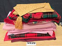 Stack of assorted linens showing gold damask runner, plaid pieces and pink cloths