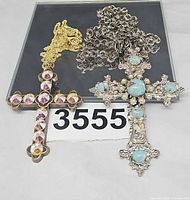 Two cross pendant necklaces laid flat showing pendants and chains