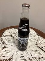 Front of sealed 10 oz Coca-Cola Dallas Cowboys Silver Season bottle on doily