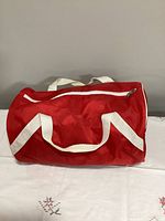 Top and side view of red gym bag showing white straps and zipper