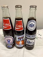 Front view of the three sealed commemorative Coca-Cola bottles showing team logos