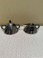 Front view of sugar bowl and creamer showing shape, handles, finials and Alessi mark