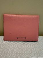Front view of pink Cole Haan pebbled leather passport holder with logo plaque