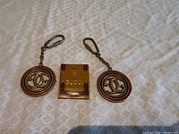 Two Gucci monogram keychains and Gucci matchbook on fabric surface