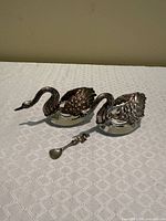Two crystal swan-form salt cellars and spoon on patterned cloth