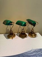 Three brass banker's lamps with green glass shades shown side by side