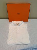 Folded white polo shirt with orange Hermès box behind