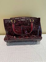 Front view of red crocodile-embossed leather handbag showing exterior pockets and handles