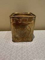 Front view of brass tea canister showing embossed TEA motif