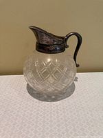 Full view of cut crystal pitcher showing spherical body, diamond pattern, silver-plated spout and handle
