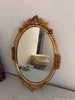 Full view of ornate gold-tone oval wall mirror on wall