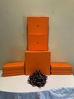 Front view showing all nine orange Hermès boxes stacked with ribbon pile