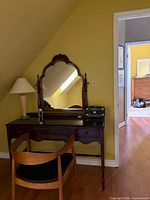 Front view of mahogany vanity table with arched mirror, chair and lamp shown for scale