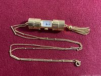 Pendant watch with chain laid out on red surface