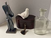 Group view showing all four items: steel sculpture, ceramic bird, wood box, glass decanter