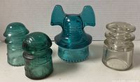 Four glass insulators lined up: aqua Hemingray 60 Mickey Mouse, two aqua dome-top pieces and clear dome-top piece