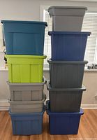two stacks of eight lidded plastic storage totes in various colors