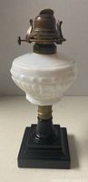 Front view showing white opalescent glass font, brass burner, black glass base