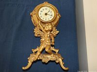 Front view of gilt mantel clock with cherub figure and dial