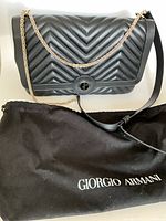 Front view of chevron-quilted bag with chain and leather straps, dust bag below