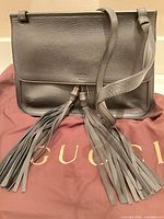 Full view of Gucci black leather bag on dust bag showing shape, strap and tassels