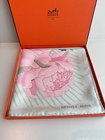 Scarf displayed in open Hermès box, showing floral design and hand-rolled edge
