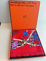 Open Hermès box displaying folded red floral silk scarf