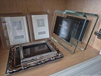 Group shot of six frames on shelf: two boxed glass, two standing Royal Doulton glass, two ornate pewter frames stacked