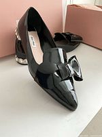Oblique view showing glossy patent leather upper, bow detail and overall style