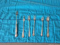 All six assorted sterling silver forks laid out on blue felt roll