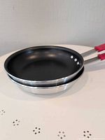 Two nested Tramontina non-stick frying pans showing exterior and interior surfaces