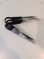 Four black-handled stainless steel cooking tongs closed together