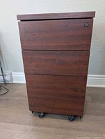 Full view of cabinet front showing wood-look finish, three drawer faces, lock cylinder, four casters