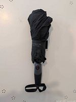 Folded umbrella showing handle, strap, brand marking