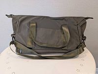 Front view of gray duffel bag, handles and shoulder strap visible