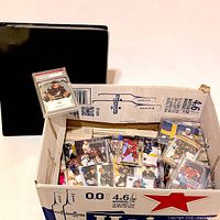 carton filled with loose hockey cards, graded card displayed, binder nearby