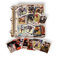 Binder opened with plastic pocket pages full of football cards; loose stacks of additional cards displayed on and in front of binder