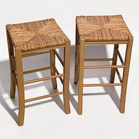Front angled view of both wooden bar stools highlighting rush seats and frame