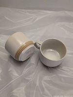 Two cream stoneware mugs, one upright one on side