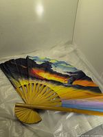 Fan fully opened showing painted ocean sunset scene and bamboo ribs
