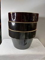 Stacked view of three brown stoneware crocks/planters showing glaze and rims