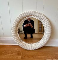 Front view of round white wicker-framed mirror leaning against wall