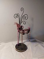 Full view of black metal jewelry holder with decorative mask and round base