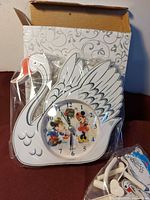 Front view of swan-shaped clock showing dial with Disney characters and original box
