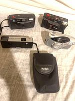 Four film cameras and Kodak pouch laid out on fabric surface